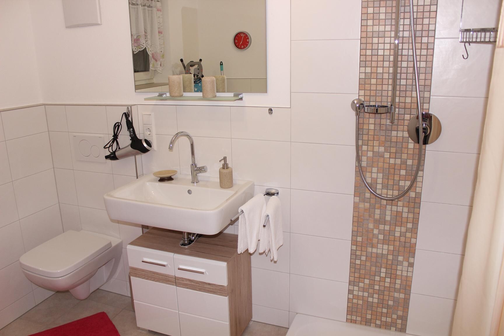 A bathroom with a white sink, a toilet, a shower with a tiled wall, and a mirror above the sink.