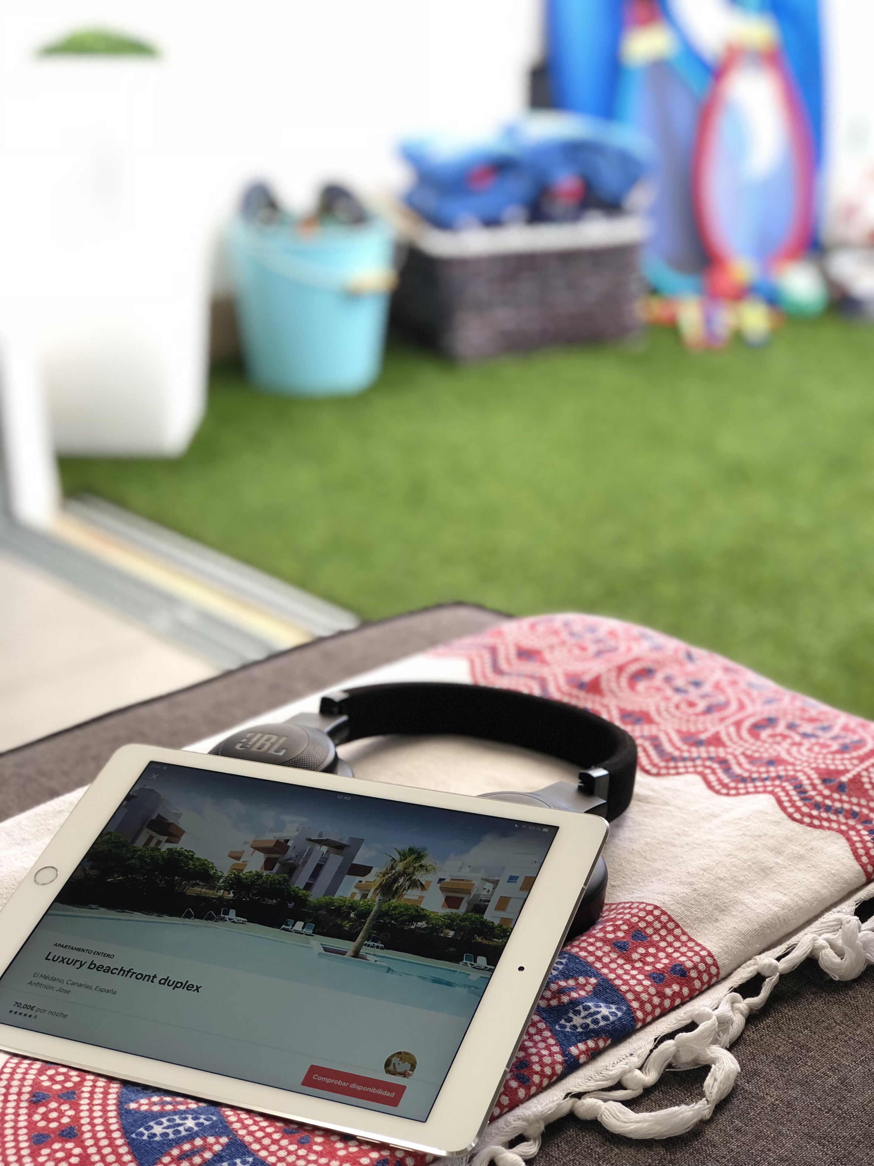 A tablet displaying a property listing for a beachfront duplex, with a pair of headphones resting on a patterned fabric.