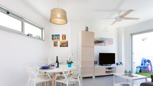 A modern living room with a dining area, a ceiling fan, and a television.
