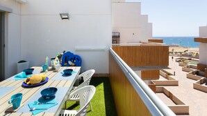 A balcony with a table set for dining, overlooking a beach.