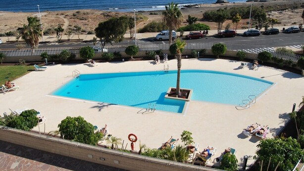 A pool area with a clear view of the ocean, surrounded by palm trees and lounge chairs.