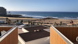 A view of a beach with a building in the background, a parking area, and a playground.