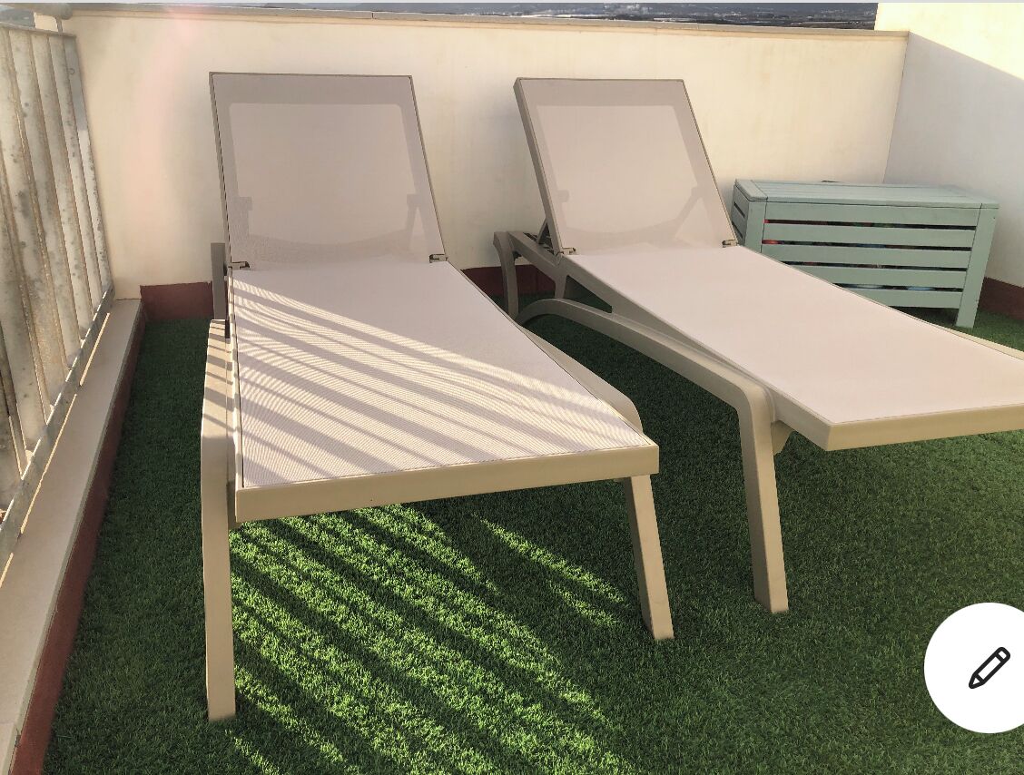 Two lounge chairs with a small table, a bench, and a green artificial turf floor.