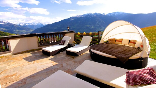 Terraza con sillones de descanso y una cama con dosel, con vista a un paisaje montañoso.