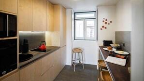 Et kompakt køkken med træskabe, en sort induktionskogetop, en rød elkedel og en lille skammel.