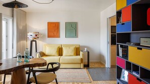 En moderne stue med et træspisebord, gul sofa, farverfuld opbevaringsenhed og abstrakt vægkunst.