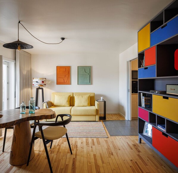 A modern living room with a wooden dining table, yellow sofa, colorful storage unit, and abstract wall art. - The ‘Story Studio’ Coimbra Centre is located in the historic area (Coimbra)