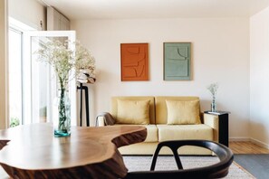 Un salon comprenant un canapé, une table ronde en bois et deux tableaux abstraits accrochés au mur.