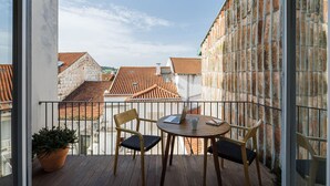 A balcony with a wooden table and chairs, a potted plant, and a view of traditional buildings with red-tiled roofs.