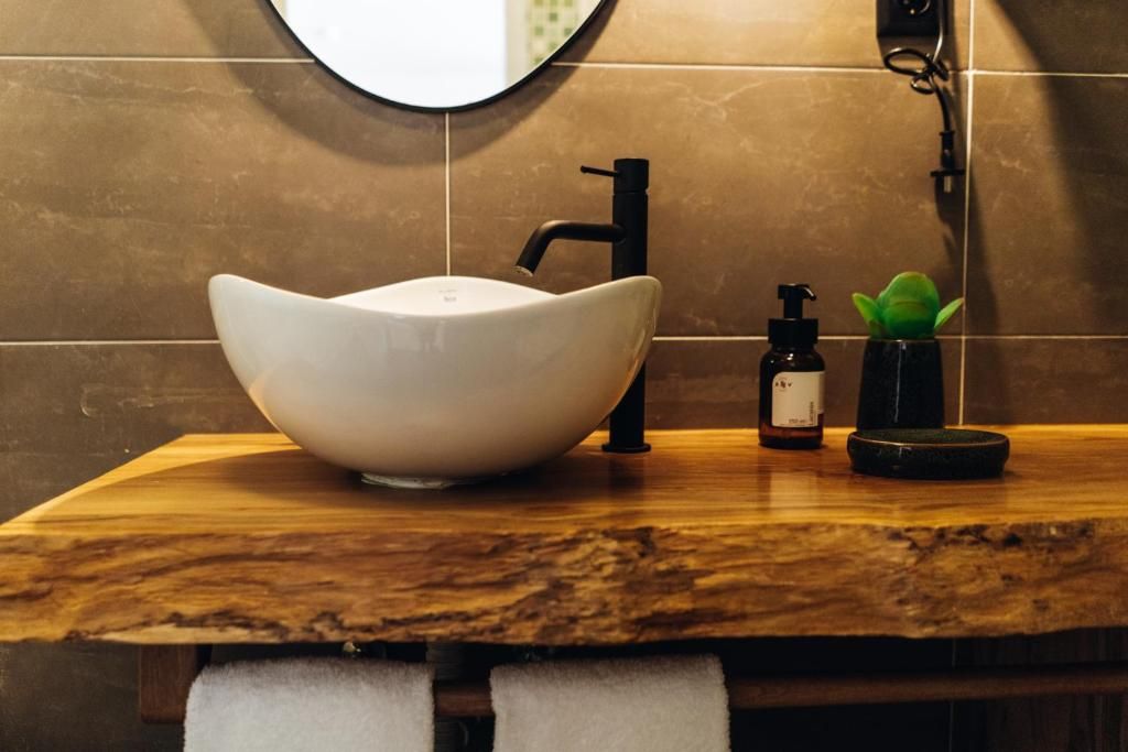 A bathroom with a white vessel sink, a black faucet, a small bottle of soap, and a green plant on a wooden countertop.