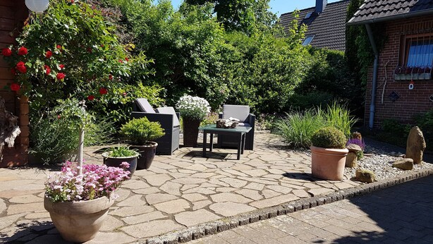 Ein Terrassenbereich im Freien mit Steinboden, Pflanzkübeln, einem Tisch und zwei Stühlen.