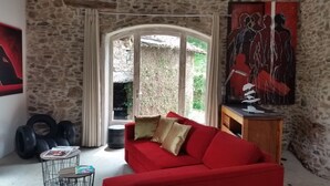 Un salón acogedor con un sofá rojo, una pared de piedra, un ventanal grande y un cuadro.