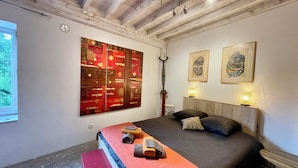 Un dormitorio con una cama grande, un banco, un reloj de pared y dos obras de arte enmarcadas.