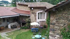 Una casa de piedra con tejado de baldosas, un pequeño jardín con mesa y sillas, y un patio con barbacoa.