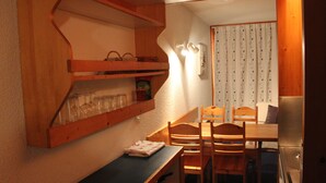 Une cuisine de taille réduite, dotée de meubles de rangement en bois, d’une table à manger avec des chaises et d’un réfrigérateur.