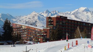 Un hôtel à étages multiples, doté de balcons, qui se dresse sur un fond de montagnes enneigées.