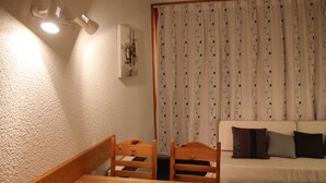 Une pièce comprenant une table et des chaises de salle à manger en bois, un canapé blanc avec des coussins, un rideau à motifs et un luminaire suspendu au plafond.