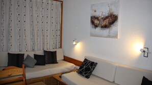Une pièce comprenant un canapé, une chaise en bois et un lit. Il y a un tableau au mur et une fenêtre avec des rideaux.