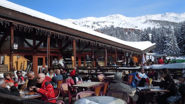 Un restaurant en plein air, avec des tables et des chaises, entouré de montagnes enneigées.