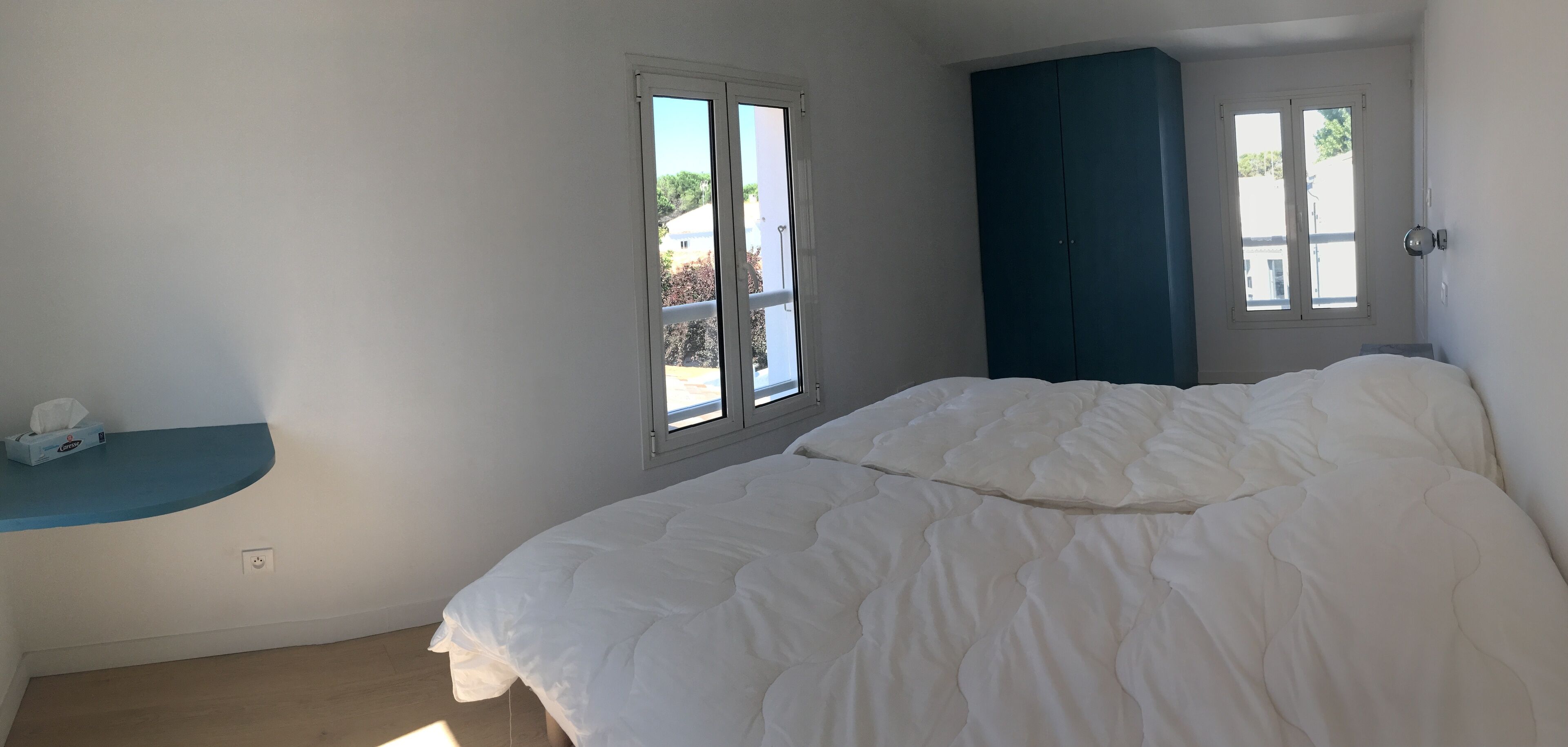 Un dormitorio con cama, ventana, armario y una pequeña estantería.