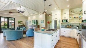A spacious kitchen with white cabinetry, a central island, and stainless steel appliances. There is a dining area with blue furniture and a large window.