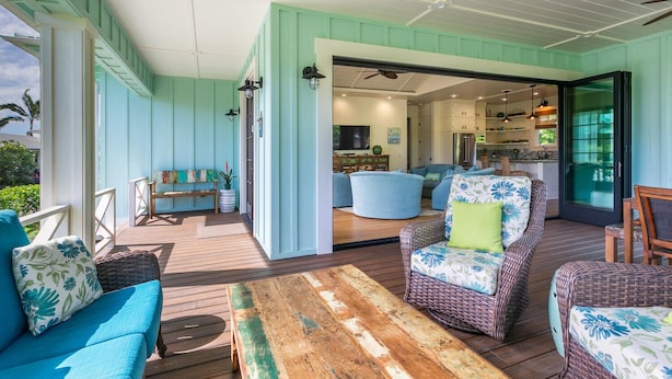 A covered outdoor area with a wooden deck, wicker furniture, and a view into the house.