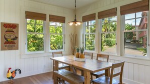 A dining area with a wooden table and chairs, large windows with wooden blinds, and a ceiling light fixture.
