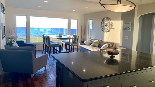 A spacious kitchen with a large island, a dining area with a view of the ocean, and a cozy seating area with a sofa and chairs. - Lake Michigan Home with gorgeous views, great spot for family or golf retreat (Sheboygan)
