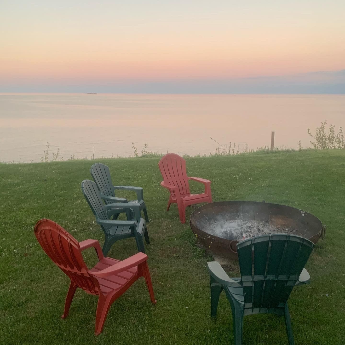 A grassy area with four Adirondack chairs and a fire pit.