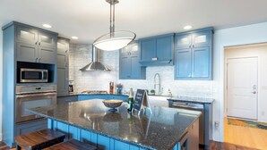 A modern kitchen with blue cabinets, a large island, stainless steel appliances, and wooden stools. - Lake Michigan Home with gorgeous views, great spot for family or golf retreat (Sheboygan)