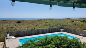 A pool area with a view of the ocean, a wooden fence, and a table and chairs.