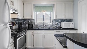 A kitchen with white cabinets, a black countertop, a microwave, and a window with a view of a house.