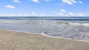 A beach with waves gently lapping onto the shore under a clear blue sky.