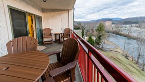 Un balcon avec des chaises et une table en bois, d’où l’on peut admirer une rivière et des collines lointaines.