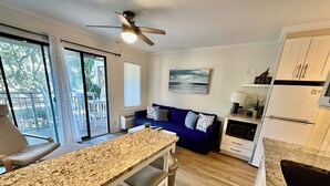 A modern kitchen with a granite countertop, a dining area with a white table and benches, a blue sofa, and a ceiling fan.