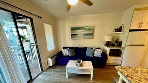 A living room with a blue sofa, a white coffee table, and a kitchen area with a refrigerator and microwave.