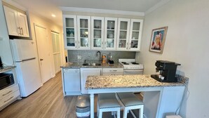 A compact kitchen with white cabinetry, a granite countertop, a stove, a sink, and a trash can.