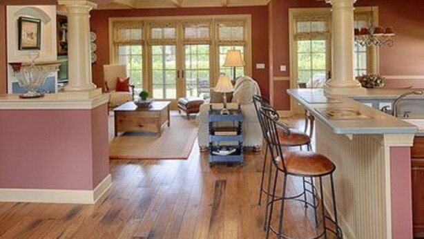 A spacious kitchen with a central island, wooden flooring, and large windows.