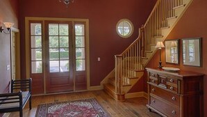 A room with a wooden staircase, a door with glass panels, a wooden dresser, and a patterned rug.