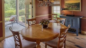 A dining area with a wooden table and chairs, a chandelier, and a painting on the wall.