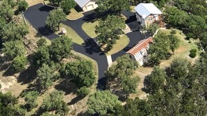 An aerial view of a residential area with multiple houses, a winding driveway, and a small pond. - VIEWS! Texas Hill Country - Bella Vista (Dripping Springs)