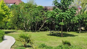 A garden with a paved path, a wooden bench, and various trees and shrubs. - Cosy duplex near Colmar and Mulhouse (Ungersheim)