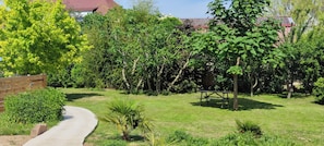 A garden with a paved path, a wooden bench, and various trees and shrubs. - Cosy duplex near Colmar and Mulhouse (Ungersheim)
