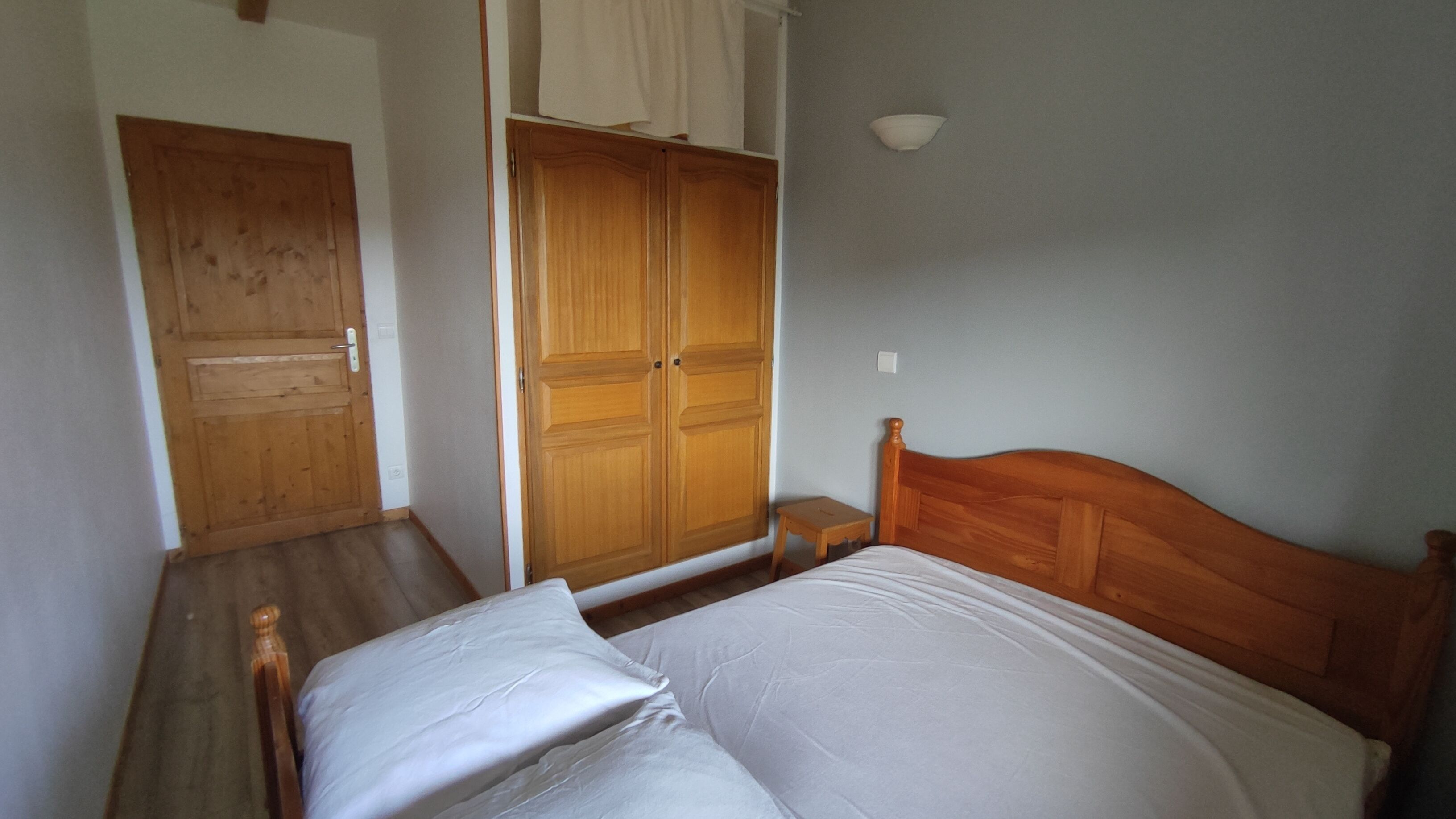 Een slaapkamer met een houten bed, een houten kledingkast en een klein nachtkastje.
