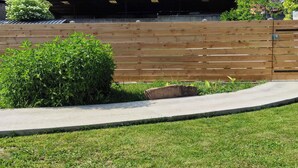 A wooden fence with a small bush in front, a concrete pathway, and a grassy area.