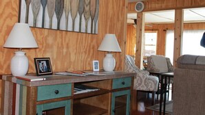 A wooden interior with a desk, two lamps, a framed photo, and patterned chairs.