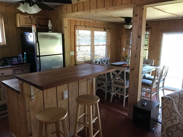 A wooden cabin-style kitchen with a central island, bar stools, and a dining area with chairs and a table.
