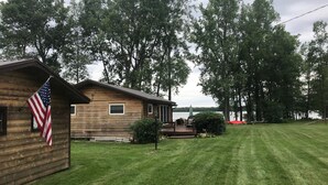 A wooden cabin with an American flag, a lawn, and trees in the background.
