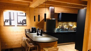 Een moderne keuken met houten wanden, een centraal eiland met barstoelen, roestvrijstalen apparatuur en hanglampen.