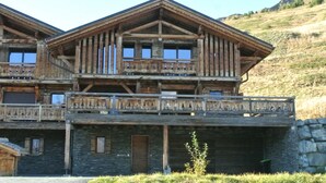 A wooden chalet with a balcony and stone foundation, set against a hillside. -  Beautiful recent chalet, very comfortable, ski IN & OUT with exceptional views (Val-d'Illiez)